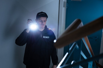 Male Security Guard Standing On Staircase Holding Flashlight