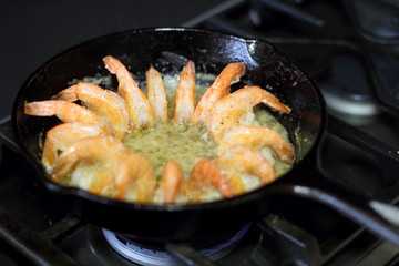 Shrimp cooking in butter and garlic in a cast iron skillet on the stove.