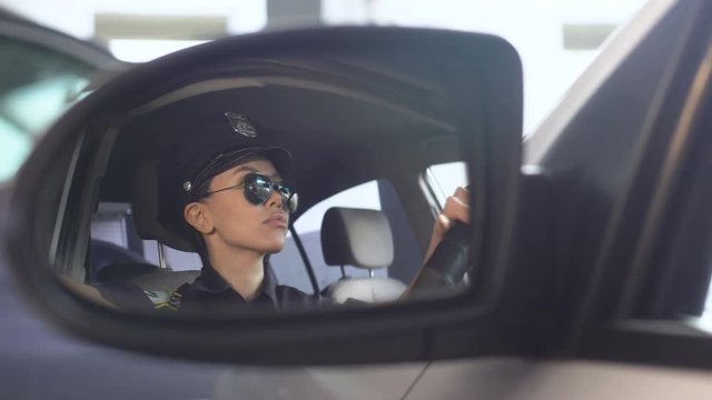 Confident policewoman putting on sunglasses looking into rearview mirror of car