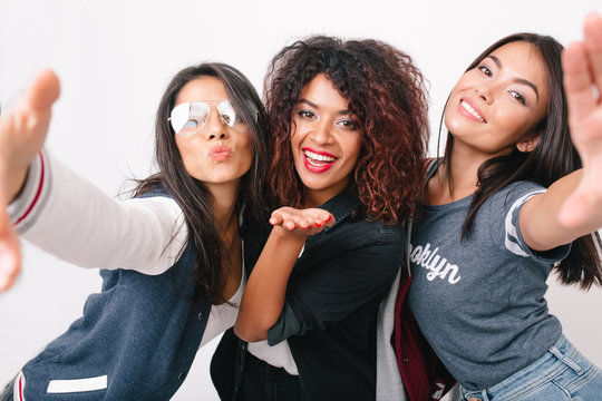 Close-up photo of smiling asian girl with tanned skin making selfie with her international friends. Excited african lady posing between charming young women in trendy clothes.