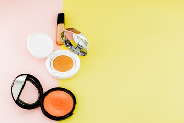 Fototapeta na wymiar Make up products spilling on to a bright yellow and pink background with copy space