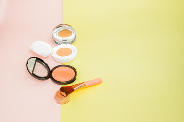 Make up products spilling on to a bright yellow and pink background with copy space