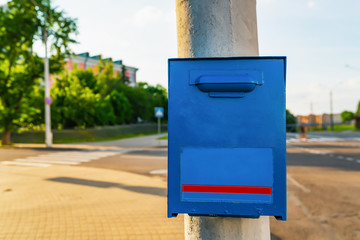 Blue painted metal mailbox front side on the grey concrete post in the city street
