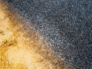 Close-up view from above of new asphalt with peace of dirt road. A smooth dark grey asphalt pavement texture with small rocks. Wallpaper and prind template.