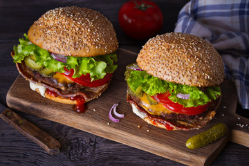 Delicious homemade beef burgers with bacon on wooden chopping board. horizontal
