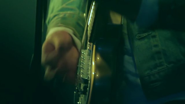 Close up of an electric guitar being played during a concert. Dim venue lighting shines on the guitar. View of artists hands strumming and playing a song for an audience. Grunge, festival scene.