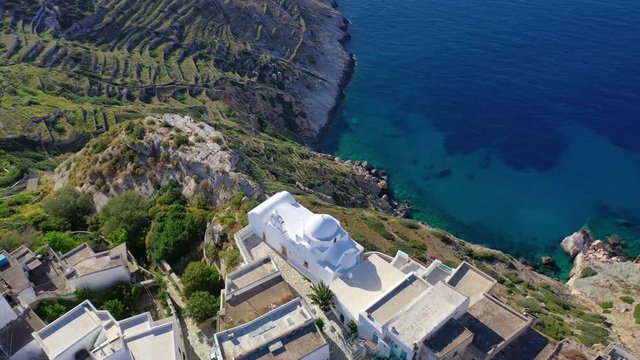 Aerial drone video of picturesque whitewashed steep cliff church of Panagia Pantanassa in main village of Folegandros island with stunning views to deep blue Aegean sea, Cyclades, Greece
