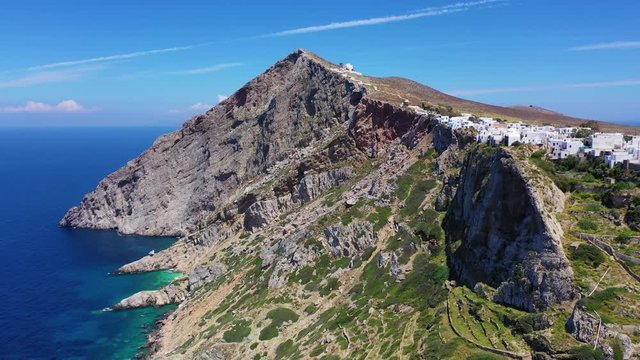 Aerial drone video of picturesque uphill church of Panagia built on a steep cliff (Virgin Mary) with stunning views to chora of Folegandros island and deep blue Aegean sea, Cyclades, Greece