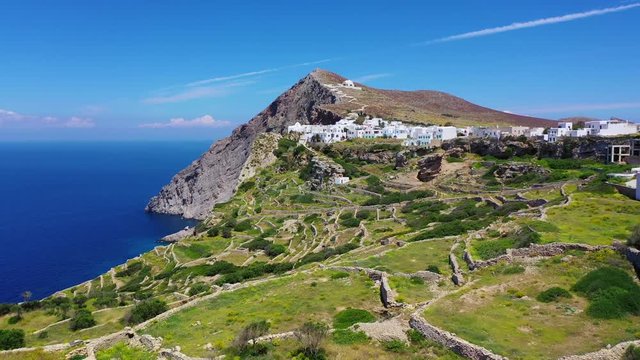 Aerial drone video of iconic and picturesque main village (chora) of Folegandros island featuring castle and built on top of steep hill overlooking the Aegean blue sea, Cyclades, Greece
