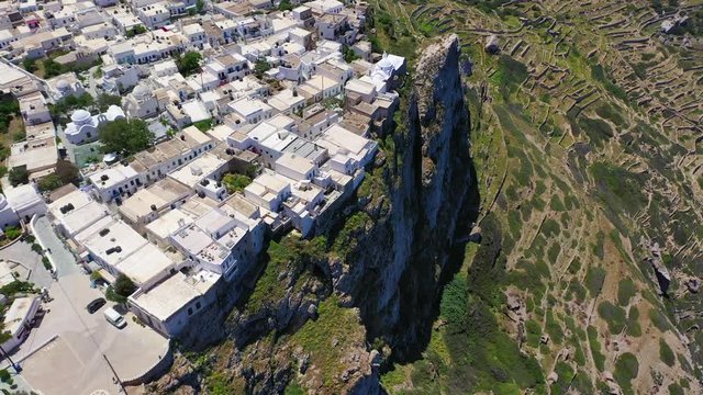 Aerial drone video of iconic and picturesque main village (chora) of Folegandros island featuring castle and built on top of steep hill overlooking the Aegean blue sea, Cyclades, Greece