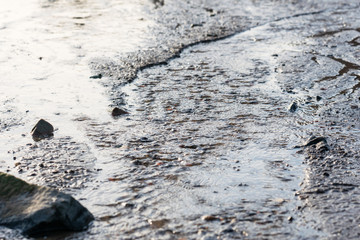 Ripples of murky water flowing along the beach on a grey, sad, moody day