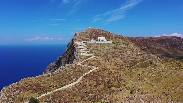 Aerial drone video of picturesque uphill church of Panagia built on a steep cliff (Virgin Mary) with stunning views to chora of Folegandros island and deep blue Aegean sea, Cyclades, Greece