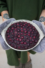 Cherry chocolate pie in non-sticky skillet. Woman holds hot tart baked in pan using the oven mitts.