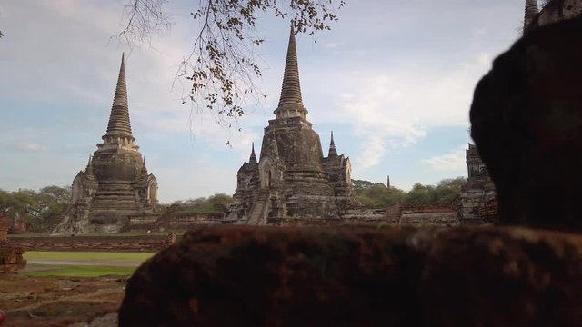 Panning shot to behind old stone ruins view of threes spiked tower pagodas, old temple Wat Ma Ha That in Ayutthaya, Thailand.