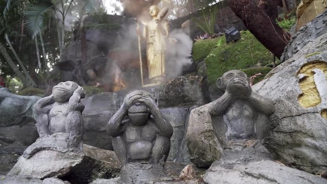 Static shot of three wise monkeys at golden mount temple Thailand, Bangkok. See no  evil, hear no evil, speak no evil statues in exterior, outside shrine with flowing misty water features.