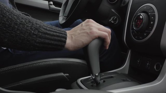 Urban man using transmission and taking steering wheel. Man hand on automatic transmission car lever. Driver man controls auto and switch gears. Close up of gear shift in car. Gearbox auto.