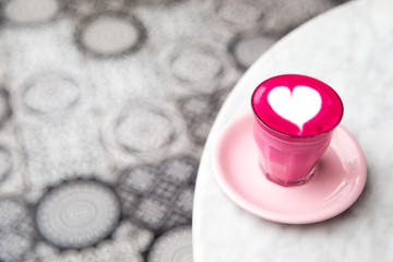 Glass of pink beetroot latte with heart latte art on marble table background.