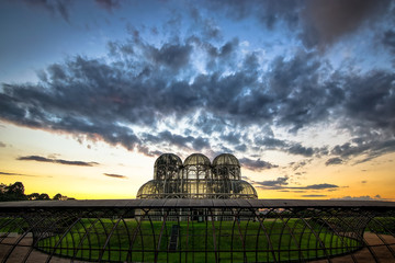 Fototapeta premium Botanical Garden of Curitiba. Beautiful day with some clouds in the sky. In the image the sunset and the greenhouse with many flowers.