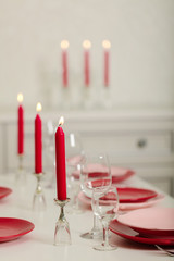 Merry Christmas and Happy New Year! Table setting - red and pink dishes, holiday knitted decor - Santa Claus knitted hats on the bottle with wine, red candles.