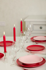 Merry Christmas and Happy New Year! Table setting - red and pink dishes, holiday knitted decor - Santa Claus knitted hats on the bottle with wine, red candles.