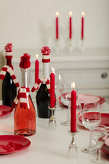 Merry Christmas and Happy New Year! Table setting - red and pink dishes, holiday knitted decor - Santa Claus knitted hats on the bottle with wine, red candles.