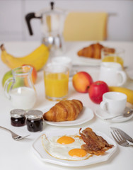 Fototapeta na wymiar Breakfast time. Fried eggs and bacon. Croissants and orange juice, jam. Coffee with cream or milk. Fruits - bananas, red and green apples.