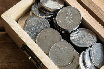 silver coins Thai Baht in toy wooden chest on wood table, close-up