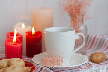 Obraz na płótnie Canvas A hot cup of black tea with homemade cookies on a striped tablecloth, wax candles, a glass vase with decorative herbs on a white background.