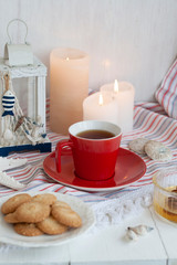 Obraz na płótnie Canvas A cup of black tea with homemade cookies on a striped tablecloth, a bowl honey, a decorative lantern, seashells; wax candles on the white background.