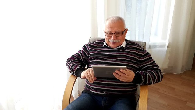 advanced old man with mustache in black sweater blue jeans sits in armchair has fun showing green screen closeup