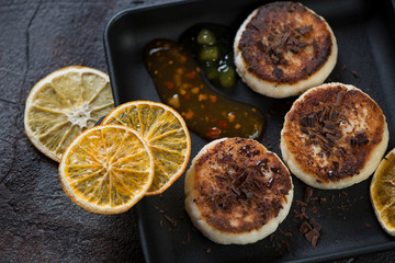 Curd pancakes or syrniki with chocolate crumbs, dipping sauce and orange chips, close-up, studio shot