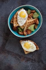 Bowl with waffles, fried eggs and vegetables, flatlay on a grey stone background with copyspace, vertical shot