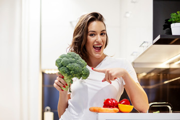 Beautiful girl in kitchen use broccoli as microphone and sing while prepare vegan fresh meal
