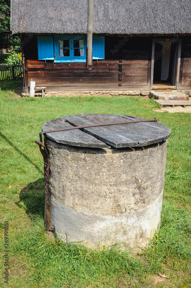 Poster Old well in front of wooden cottage in heritage park in Olsztynek town of Olsztyn County in Warmia-Mazury Province, Poland