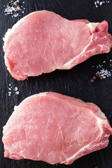 Top view of two pieces raw  pork  chop steaks with salt and pepper on a black. Closeup