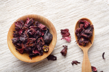 Top view at wooden bowl and spoon of dry hibiscus petals on linen cloth background