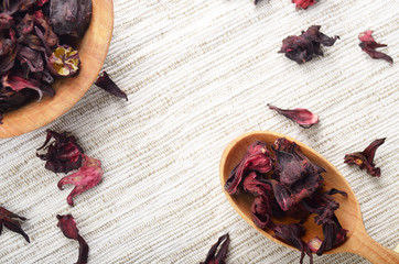Top view at wooden bowl and spoon of dry hibiscus petals on linen cloth background