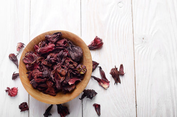 Top view at wooden bowl of dry hibiscus petals on white background