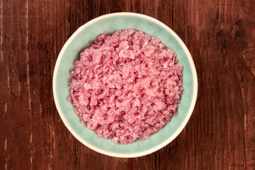 A bowl of pink Himalayan sea salt, shot from above on a dark rustic wooden background