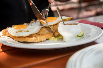 Mann isst Schweine Fleisch Schnitzel Wiener Art mit Spiegelei als Hamburger dazu Gurken Kartoffelsalat und Bayrischen süßen Senf im Biergarten Restaurant