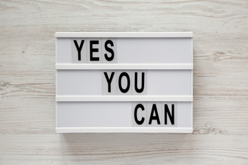'Yes you can' words on a lightbox over white wooden background, top view. Overhead, from above. Flat lay. Close-up.