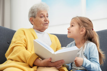 Fototapeta premium Cute girl and her grandmother reading book at home