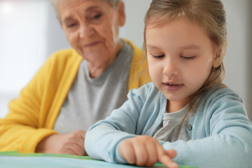 Cute girl and her grandmother reading book at home