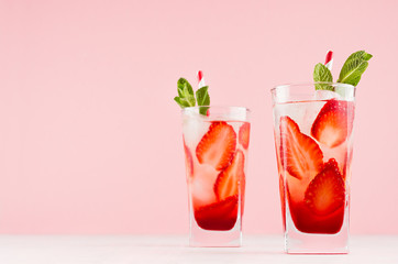 Summer strawberry lemonade with green mint, ice cubes, striped straw on elegant pastel pink wall, white wood table, copy space.