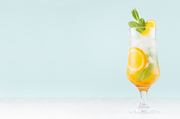 Fresh orange cocktail with slices fruits, mint, straw, ice cubes in misted glass on white wood table and blue color wall, copy space.