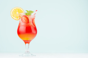 Summer oranges alcohol drink sunrise with orange, ripe sliced strawberry, ice cubes, mint in misted...