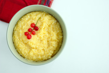 View from above of maize porridge in bowl with branch red currant on it served with red napkin on...
