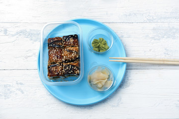 portion of rolls with eel with wasabi and ginger on a plastic blue plate on a white table