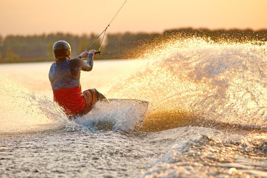 Low angle shot of man wakeboarding on a lake. Man water skiing at sunset. Wakeboarder making tricks 
