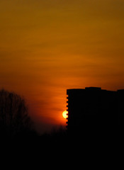 Fototapeta premium The black silhouette of the house against the bright orange sunset. The sun is setting beautifully. The view of the sunset.